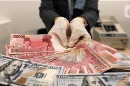 Tangan memegang Dolar AS pecahan $100 di atas tumpukan Rupiah Rp100.000, transaksi valuta asing.