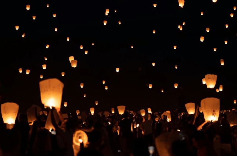 Kerumunan orang di bawah menerbangkan banyak lampion terbang yang telah mengisi langit malam