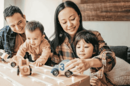 Keluarga muda bermain bersama anak-anak di rumah, menggambarkan kebahagiaan dan perlindungan melalui asuransi kesehatan keluarga.