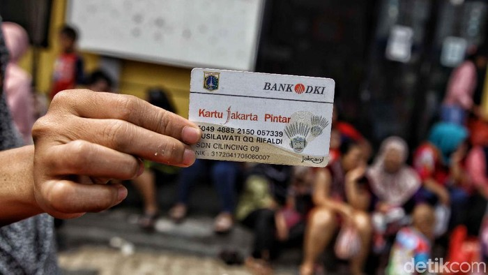 Seorang anak atau orang tua memegang Kartu Jakarta Pintar (KJP) dari Bank DKI di depan kerumunan orang