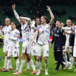 Sekelompok pemain timnas sepak bola Amerika Serikat berdiri di lapangan, mengangkat tangan dan bertepuk tangan untuk merayakan kemenangan atau hasil positif.