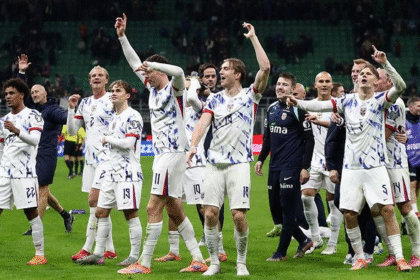 Sekelompok pemain timnas sepak bola Amerika Serikat berdiri di lapangan, mengangkat tangan dan bertepuk tangan untuk merayakan kemenangan atau hasil positif.